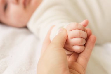 Yeni doğmuş bebeklerin küçük elleri. Beyaz tulumlu küçük bebek yatakta uzanıyordu. Yeni doğmuş bir bebeğin beyaz, sıcak bir battaniyenin üzerindeki görüntüsü. Yeni doğan uyandı ve evin içine bakıyor.