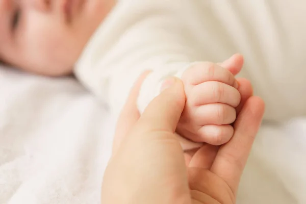 Pequenas mãos de recém-nascido. Bebé recém-nascido num fato branco deitado na cama. Vista superior de um bebê recém-nascido em um cobertor quente branco. O recém-nascido está acordado olhando em volta dentro de casa — Fotografia de Stock