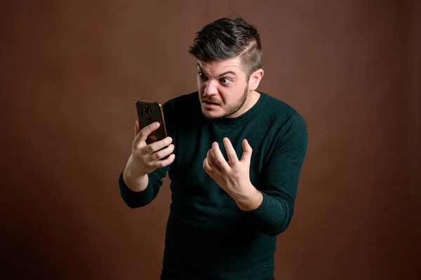 Man with brown hair looks at the phone and become angry