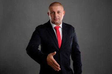 Zarif siyah takım elbise ve kırmızı kravat takan havalı iş adamının portresi gri arka planda izole edilmiş.