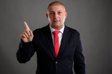 Zarif siyah takım elbiseli havalı iş adamının portresi ve gri arka planda izole bir yer göstermeyen kırmızı kravat.