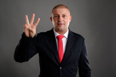 Zarif siyah takım elbiseli havalı iş adamının portresi ve gri arka planda üç izole edilmiş kırmızı kravat.