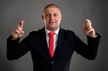 Zarif siyah takım elbiseli ve kırmızı kravatlı havalı iş adamı gri arka planda çift iyi şanslar gösteriyor.