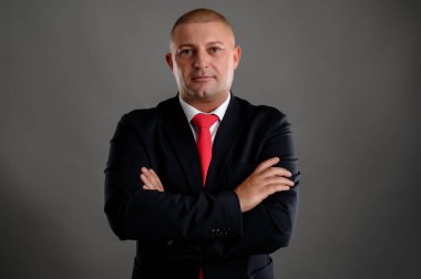 Zarif siyah takım elbiseli ve kırmızı kravatlı havalı iş adamının portresi gri arka planda izole edilmiş güveni gösteriyor.