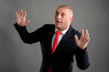 Korkmuş adamın portresi, siyah takım elbiseli ve kırmızı kravatlı iş adamı gri arka planda izole edilmiş sahte bir yemin gösteriyor.