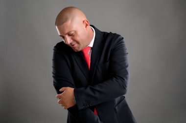 Zarif siyah takım elbiseli ve kırmızı kravatlı havalı iş adamının portresi gri arka planda izole edilmiş sıkı çalışmadan dolayı dirsek ağrısı çekiyor.