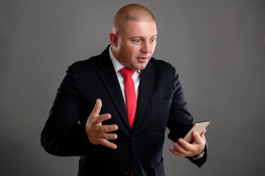 Zarif siyah takım elbise ve kırmızı kravat takan havalı iş adamının portresi. Davranışları vahşileşiyor ve elleri gri arka planda izole bir şekilde el kol hareketi yapmaya başlıyor.