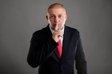 Zarif siyah takım elbiseli ve kırmızı kravatlı havalı iş adamının portresi parmaklarını dudaklarına koyuyor, sanki 