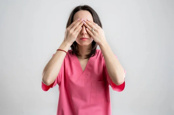 Young woman medical professional nurse or doctor dressed with pink hospital clothes, with brown hair, in the see no Evil posing on a white isolated backround.