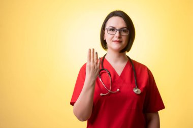 Steteskoplu güzel kadın doktor portresi kırmızı önlük giyiyor, sarı izole edilmiş arka planda parmaklarıyla dört tane sayıyor..