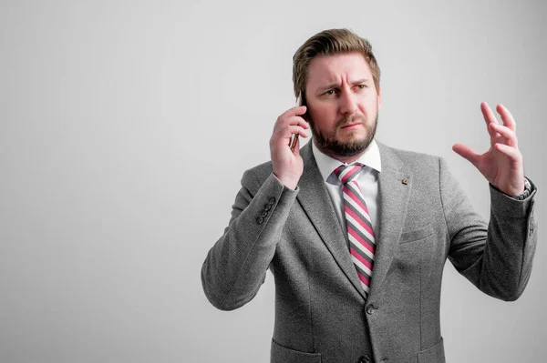 Portrait of angry business man wearing business clothes talking on the phone isolated on grey background with copy space advertising area