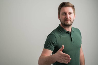 Kalın sakallı, ciddi şekilde şık ve çekici bir adamın portresi. Günlük yeşil tişörtler giyip el sıkışıyor. Gri arka planda, fotokopi alanı reklam alanı ile izole edilmiş.