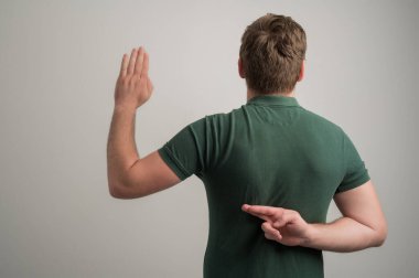 Kalın sakallı, sıradan yeşil tişörtlü, gri arka planda izole edilmiş fotokopi alanı reklam alanında parmaklarını gösteren ciddi stil sahibi çekici bir adam.