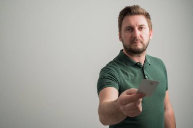 Kalın sakallı, sıradan yeşil tişörtlü ciddi tarz çekici bir adamın portresi. Gri arka planda izole edilmiş fotokopi alanı reklam alanı olan kartı ver.