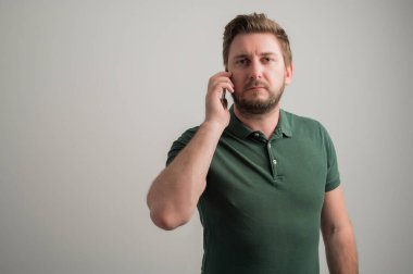 Kalın sakallı, sıradan yeşil tişörtlü, gri arka planda izole edilmiş, fotokopi alanı reklam alanında konuşan ciddi ve şık çekici bir adamın portresi.