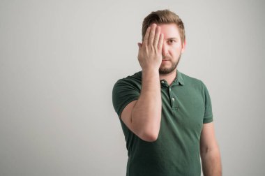 Kalın sakallı, sıradan yeşil tişörtlü, bir gözü gri arka planda, reklam alanının fotokopisi ile izole edilmiş ciddi ve şık çekici bir adamın portresi.