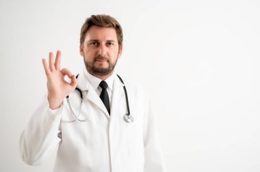 Üzerinde steteskop olan erkek doktorun portresi beyaz izole bir arka planda tamam işareti gösteriyor.