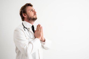 Tıbbi üniformalı erkek doktorun portresi beyaz izole bir arka planda dua ediyor..