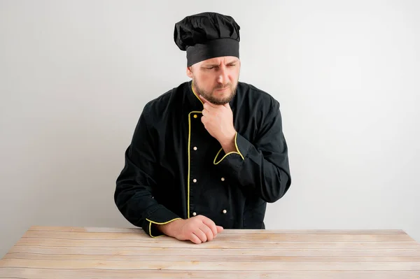 Portrait of young male chef in black uniform with open arms looking up, has sore throat posing on a white isolated background