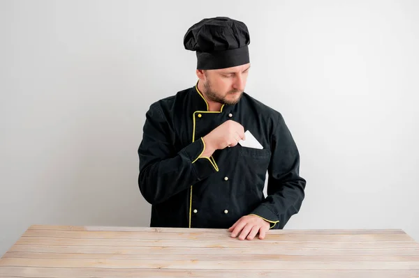 Portrait of young male chef in black uniform pull out card from her pocket posing on a white isolated background