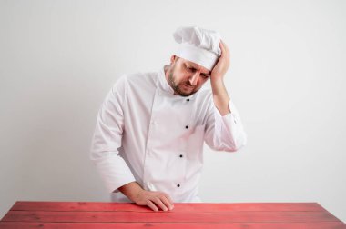 Beyaz üniformalı genç aşçının portresi, kolları açık yukarı bakıyor, beyaz izole bir arka planda baş ağrısı var.