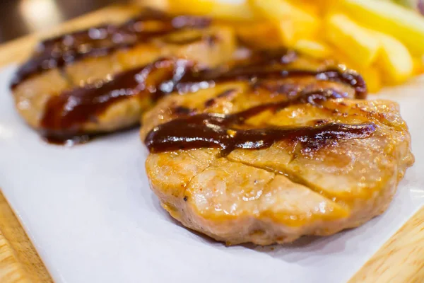 Cerdo a la parrilla con papas fritas y ensalada en plato de madera — Foto de Stock