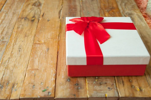 Beyaz hediye kutusu ve alan ahşap zemin üzerine kırmızı kurdele — Stok fotoğraf