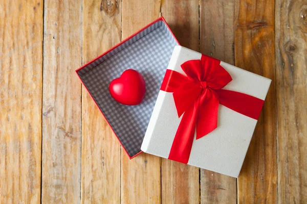 Белая подарочная коробка и красная лента и мини-сердце внутри на деревянной спине — стоковое фото