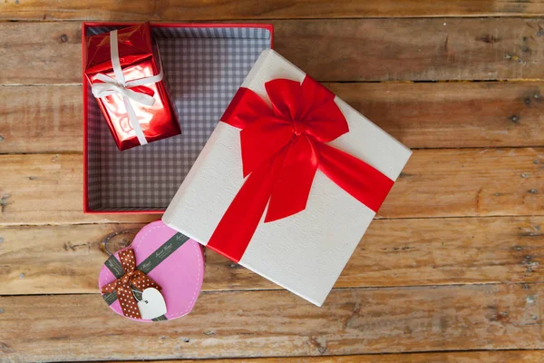Witte geschenkdoos en rood lint en mini hart binnen op hout terug — Stockfoto
