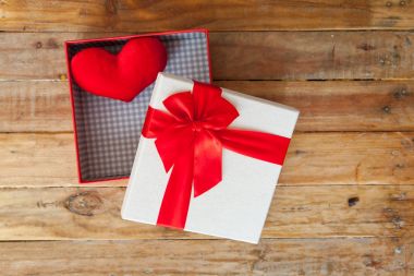 Beyaz hediye kutusu ve kırmızı kurdele ve geri ahşap üzerine mini kalp içinde