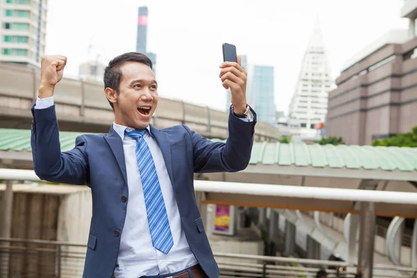 Businessman raising his fist  in the air while looking on mobile