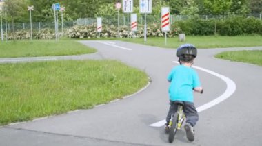 Bisiklet kasklı küçük çocuk trafik parkında denge bisikleti sürmeyi öğreniyor.