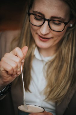 Çok zeki, gözlüklü, gülümseyen bir kadın kahve içiyor, kafede kremalı kakao içiyor.