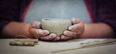 Elleri kilden yapılmış bir kase tutuyor. Panorama, alanın derinliği