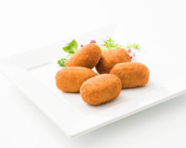 Beyaz arka planda kare seramik tabağa yerleştirilmiş bitkilerle bir sürü lezzetli kroket.