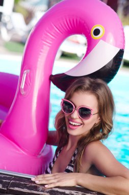 Genç ve güzel kadın çizgili mayo ve şişme bir pembe flamingo yaz ile havuzda yüzme güneş gözlüğü
