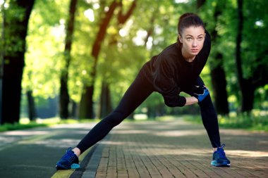 Çekici ve güçlü bir kadın yaz parkında spor öncesi esneme hareketleri yapıyor. Spor konsepti. Sağlıklı yaşam tarzı