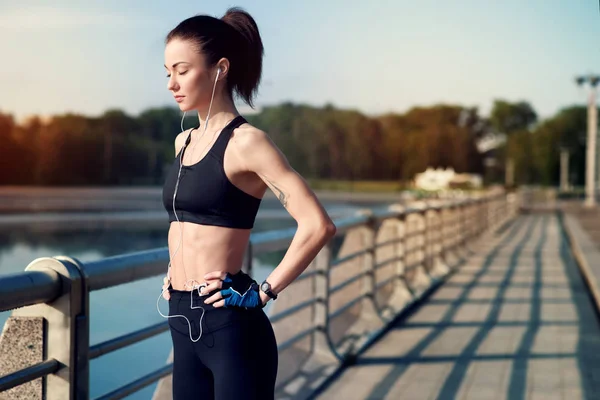 Genç ve güzel kız sporcu eğitim ve kulaklıklar müzik yaz aylarında gölde dinlemek için hazırlanıyor. Spor kavram. Sağlıklı yaşam tarzı