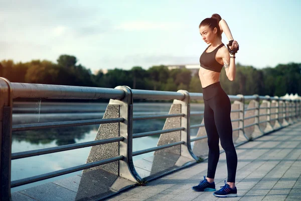Çekici ve güçlü bir kadın fitness yaz aylarında göl üzerinde önce germe. Spor kavram. Sağlıklı yaşam tarzı