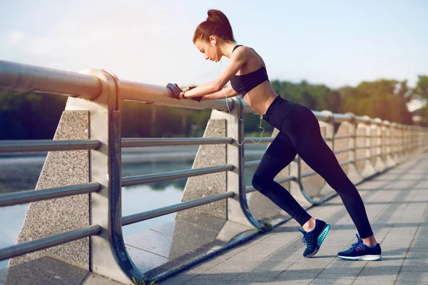 Önce Fitness germe ve yaz aylarında göl üzerinde kulaklık ile müzik dinlemek çekici ve güçlü bir kadın. Spor kavram. Sağlıklı yaşam tarzı