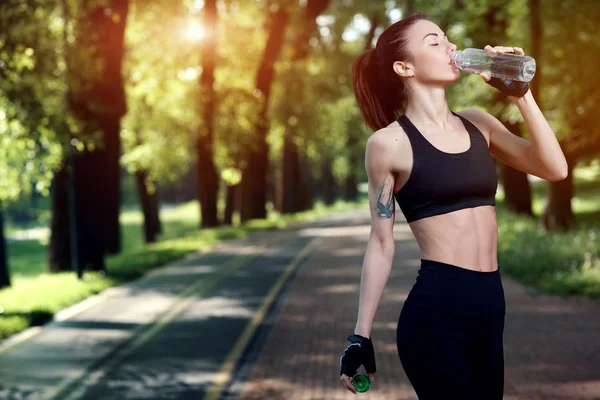 Yaz parkta genç güzel ve güçlü kız içecekler su aktif egzersiz sonrası. Spor kavram. Sağlıklı yaşam tarzı