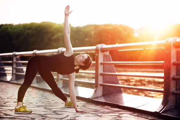 Beautiful young girl practicing yoga at sunset in the summer in the city park near the lake — Stock Photo, Image