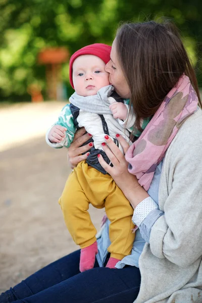 Young and happy mother cares for her young son and kisses him and plays in the summer in the park. family Concept — Stock Photo, Image