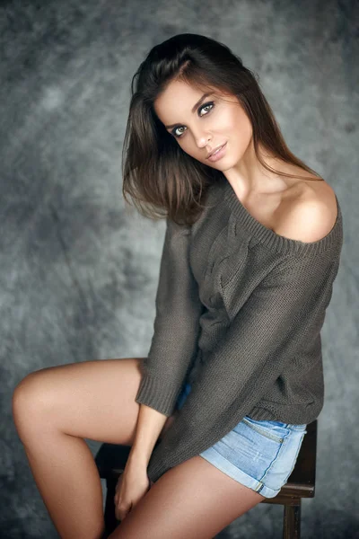 Vacker och sexig tjej i en tröja och denim shorts som sitter på en stol — Stockfoto