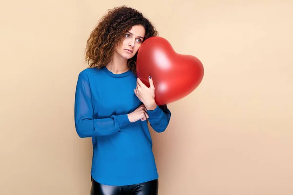 Bella ragazza con i capelli ricci e maglione blu in possesso di un palloncino rosso cuore aria. Il concetto di San Valentino — Foto Stock