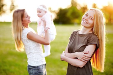 İki genç anne bebeği ile yaz aylarında parkta yürüyorlar. LGBT lezbiyen çift. Aile ve sağlıklı yaşam kavramı