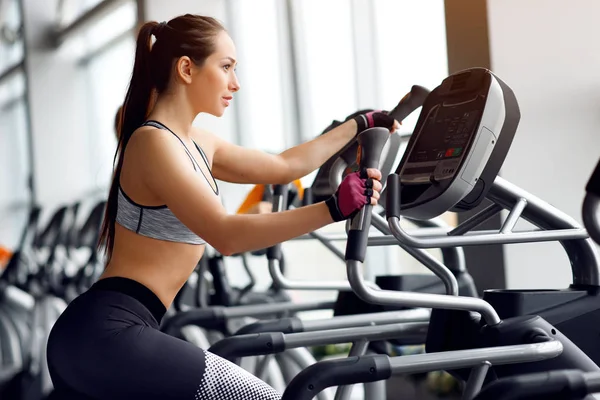 Spor ve sağlıklı yaşam kavramı. Güçlü genç güzel kadın bir spor salonu bir elipsoid üzerinde çalışmaktadır