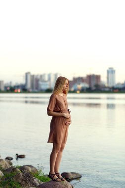 Kentsel peyzaj arka planda göl kıyısında yaz aylarında duran genç güzel hamile kadın