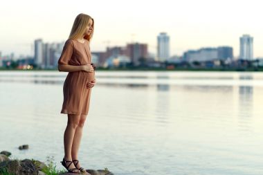 Kentsel peyzaj arka planda göl kıyısında yaz aylarında duran genç güzel hamile kadın