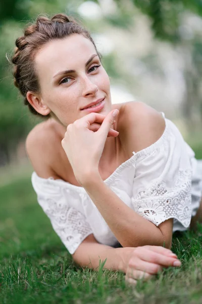 Молодая красивая сексуальная девушка лежит на траве в парке и отдыхает. Прекрасная здоровая улыбка. Причудливая прическа. Счастливая девушка — стоковое фото